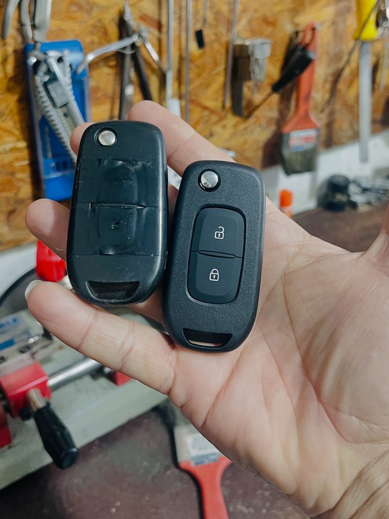 Duas chaves canivete automotivas na mão, com a parede de ferramentas da oficina ao fundo